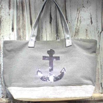 Graue Shoppertasche mit silbernem Pailletten-Anker, weißem Boden mit Silberstreifen und grauen Kunstleder-Griffen vor rustikalem Holzhintergrund.